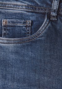 Dżinsy w ciemnoniebieskim odcieniu, z małą kieszonką z przodu, widocznym przeszyciem i gładką fakturą. Akcentowane metalowym wkrętem.