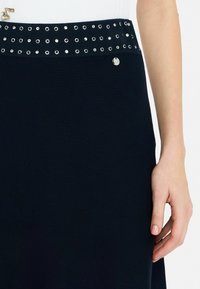 Gonna blu navy con texture a coste, caratterizzata da una cintura decorativa con occhietti d'argento e un accento in metallo con logo.