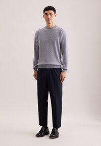 Grauer Strickpullover mit Rundhalsausschnitt, kombiniert mit marineblauen geraden Hosen und schwarzen Schnürschuhen. Glatte Texturen und einfaches Design.