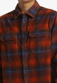 Rød og sort ternet flannel skjorte med blå accenter, der har to brystlommer, knaplukning og struktureret stof.