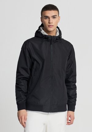 Giacca nera con cappuccio, dotata di zip frontale, polsini elastici e cappuccio con coulisse. Realizzata in materiale sintetico leggero.