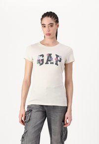 Kreminė trumpų rankovių marškinėliai su juodu "GAP" logotipu, papuoštu spalvingais gėlėmis. Minkšta medvilnė, prigludusi forma.