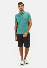 Turkusowa polo z fakturą z trzema guzikami, w połączeniu z ciemnymi szortami cargo i białymi trampkami. Prosty, casualowy styl.
