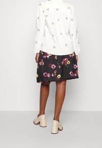 Vit blus med blommig broderi, tillsammans med en svart kjol med en färgglad blommig tryck. Beiga klackskor med tjock klack avslutar looken.