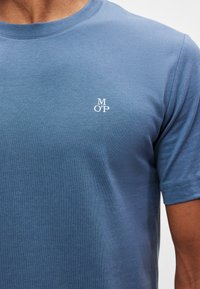 Zils kokvilnas t-krekls ar apaļu izgriezumu un īsām piedurknēm. Kreisajā krūšu daļā mazs balts "MOP" logotips. Gluda tekstūra.