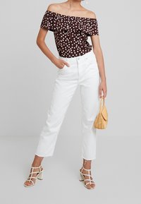 Ruskipisteinen olkaimeton toppi, valkoiset korkeat farkut ja valkoiset remmisandaalit; käsissä pieni kudottu beiget laukku.