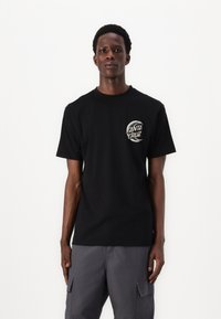 Schwarzes Baumwoll-T-Shirt mit kurzen Ärmeln und rundem Ausschnitt, versehen mit einem runden "Santa Cruz"-Logo, das auf der linken Brust gedruckt ist.