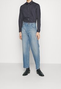 Mörkblå skjorta med knappar och ett geometriskt mönster, i kombination med ljusblå raka jeans i denim och svarta ankelstövlar.