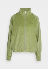 Lyst grøn kordfløjl jakke med høj krave, lynlås lukning og elastiske manchetter. Har et diskret Nike AIR-logo på brystet.