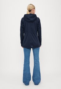 Veste à capuche bleu marine avec une taille cintrée, dotée d'une coupe droite et de manches longues, assortie de jeans en denim évasés.