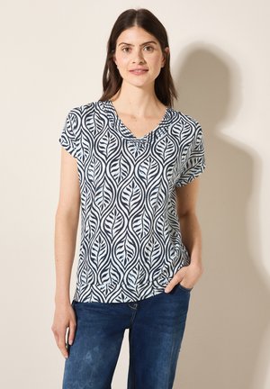 Haut à manches courtes en tissu léger avec un motif de feuilles bleu marine et blanc, doté d'un décolleté en V et d'une coupe décontractée, associé à un jean bleu.