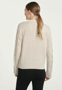 Beżowy sweter dzianinowy z rękawami w splot kablowy i ściągaczem u dołu. Widok z tyłu pokazuje luźny krój i długie rękawy.