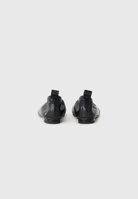 Chaussures en cuir noir avec une texture lisse, bout arrondi, talon bas et languettes à l'arrière, présentant un design minimaliste.