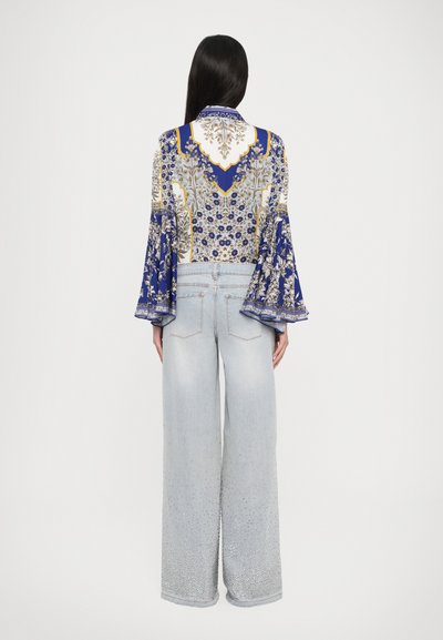 Bluză albastră cu mâneci lungi și imprimeu floral, cu mâneci tip clopot, asortată cu blugi largi din denim deschis, cu margini brodate și un fit relaxat.