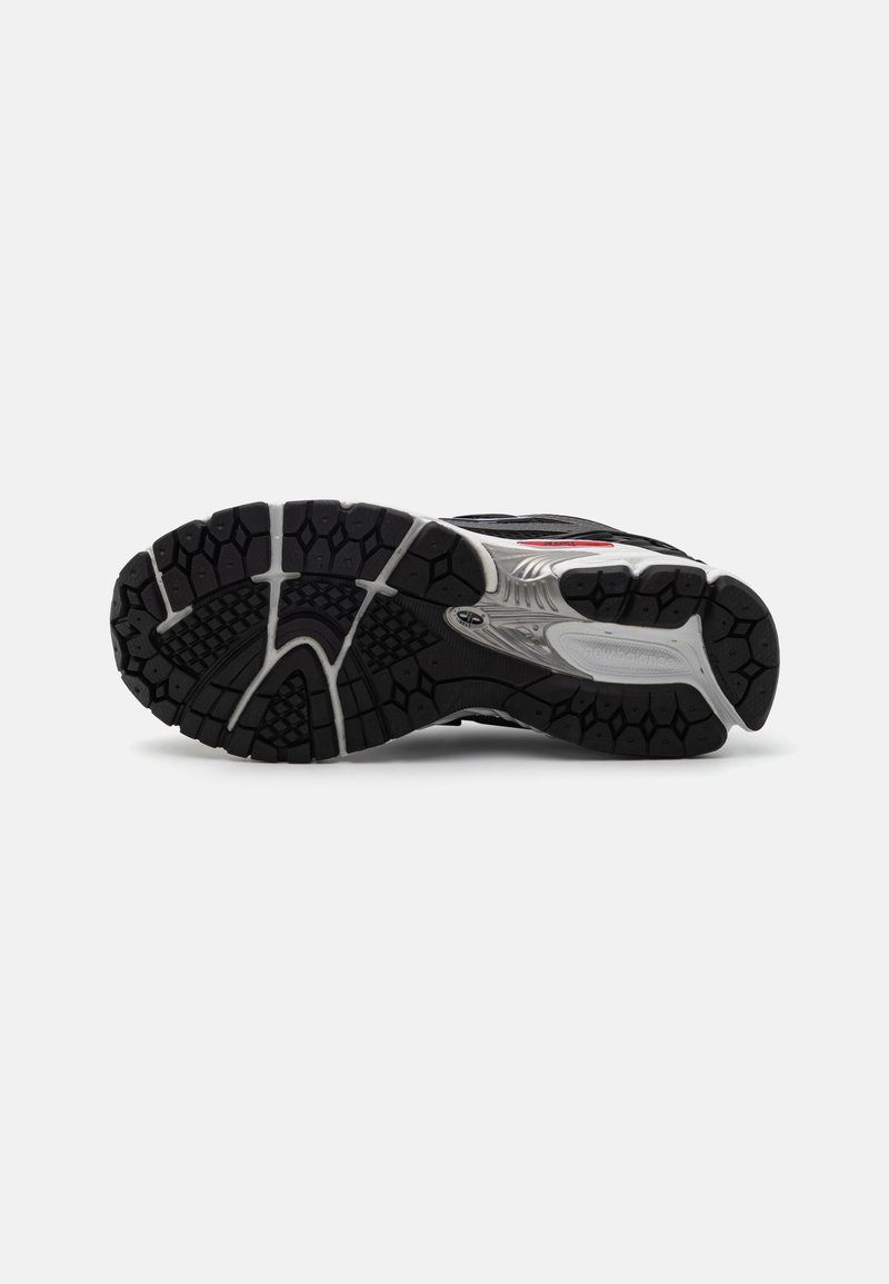 Suela de zapato deportivo negro con banda de goma texturizada. Presenta un talón reforzado, acentos plateados y un diseño en patrón para mayor agarre.