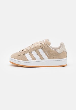 Beige ruskinn sneakers med hvite lærstriper, avrundet tå, flat hvit såle og beige snøringer. Har "CAMPUS" merkevare på siden.
