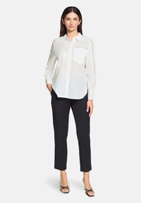 White button-up shirt with a single breast pocket, paired with black pants featuring subtle embellishments, and black strappy sandals.