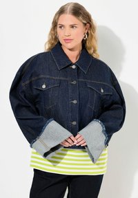Jeansjack met oversized mouwen en lichtgrijze manchetten, voorzien van zilveren knopen en twee voorkanten zakken. Draag het over een groen en wit gestreepte top.