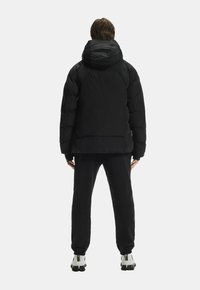 Melnā polsterētā jaka ar kapuci, kurai ir gluda tekstūra un kroptais dizains. Valkā ar saskaņotām melnām biksēm un baltām apaviem.