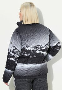 Chaqueta de plumas en blanco y negro con un patrón de montañas, tela texturizada y un cuello alto. Presenta un dobladillo y puños acanalados para mayor calidez.