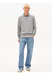 Grauer Sweatshirt mit Reißverschluss und gerippten Bündchen, kombiniert mit hellblauen Straight-Leg-Jeans und blauen Sneakern mit Gummisohle.