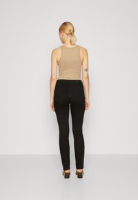 Jeans negros ajustados de cintura alta, combinados con una camiseta sin mangas beige. Los jeans tienen bolsillos traseros y se ajustan ceñidamente desde la cintura hasta el tobillo.