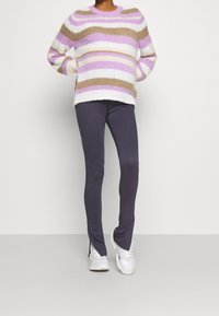 Dzianinowy sweter w kremowe, liliowe i beżowe paski; w zestawieniu z szarymi legginsami i białymi trampkami. Sweter ma szeroki dekolt i prążkowaną fakturę.