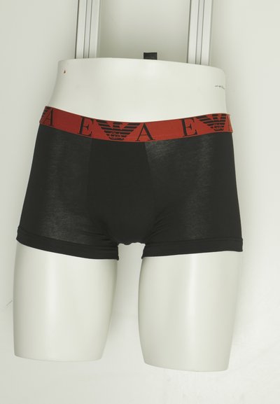 Boxer briefs negros con una cintura elástica roja que presenta un logo. El material es suave y el diseño es ajustado.