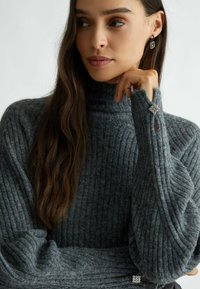 Maglione grigio a collo alto in morbida lana, con maniche ampie e un accento decorativo in argento sui polsini.