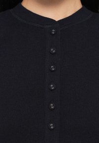 La cardigan a coste blu navy con scollo rotondo e sei bottoni di chiusura sul davanti, caratterizzata da bottoni rotondi con dettagli in metallo.