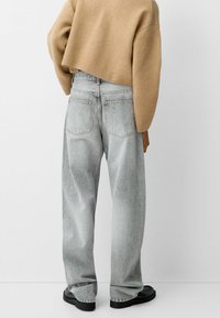 Helle graue, hoch geschnittene Jeans mit geradem Bein, ausgestattet mit zwei Gesäßtaschen und subtilen Ausbleichungen, kombiniert mit einem cropped, hellbraunen Pullover.