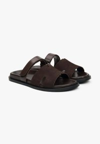 Brown suede sandals with two wide straps and an open toe design, featuring a textured surface and a flat rubber sole.