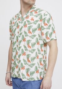 Kurzarm-Hemd mit Knöpfen aus einem cremefarbenen Stoff, verziert mit einem bunten Print von orangefarbenen Flamingos und grünen Blättern.
