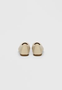 Beežilised libisevad kingad, mille eespool on tekstureeritud kootud kangas ja tagaküljel sile nahk, pruuni kummist tallaga ja ümarate varvaste kujundusega.