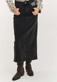 Černá džínová sukně s př ímým střihem, dlouhou délkou, předními kapsami a dekorativním prošíváním. Kombinováno s hnědými semišovými kotníkovými botami.