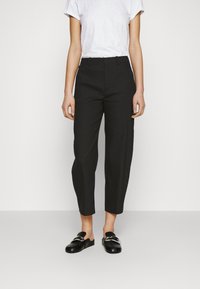 Zwarte cropped broek met een getailleerd ontwerp, voorzien van een gladde textuur en hoge taille. Gecombineerd met een simpele witte T-shirt en zwarte schoenen.