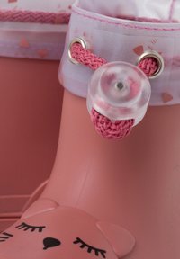 Scarpa di gomma rosa con design di faccia d'orso, lacci intrecciati rosa, bottone trasparente e motivo decorativo a cuori sul bordo superiore.