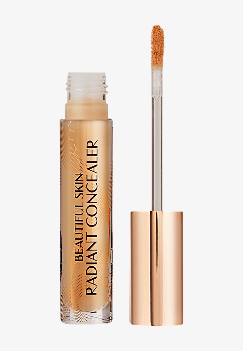 Correcteur liquide dans un tube transparent avec des accents dorés. Il dispose d'un applicateur doux et d'une teinte beige chaud. Marquage texturé visible.