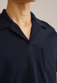 Polo majica s kratkimi rokavi v mornarsko modri barvi, izdelana iz mehke tkanine, z zloženim ovratnikom, brez gumbov in žepom na prsih.