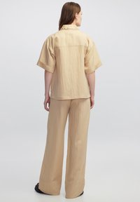 Conjunto de dos piezas en color beige claro, hecho de una tela texturizada, que incluye una camisa de manga corta y pantalones de pierna ancha con un ajuste relajado.