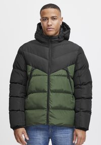 Sort og grøn pufjakke med lynlås foran, hætte og chevrondesign. Har lynlåslommer og en puffy tekstur. Justerbar hætte.