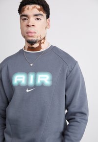 Gray sweatshirt made of soft fabric featuring a large, stylized "AIR" logo in blue and white, with a Nike swoosh at the bottom.
