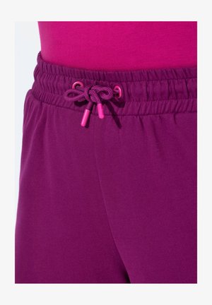 Violet jogger-housut, joissa on teksturoidut vyötärönauhat ja vaaleanpunaiset nyöritysnipukkeet. Sujuva kangas, tiiviisti istuva malli.