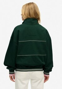 Donkergroene oversized sweatshirt met hoge kraag, witte accenten in de vorm van strepen over de rug en geribde manchetten. Zachte stof met een relaxte fit.