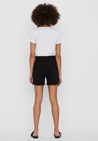 Shorts noirs avec une taille élastique et deux poches latérales, associés à un t-shirt blanc. Le tissu semble lisse avec une coupe décontractée.