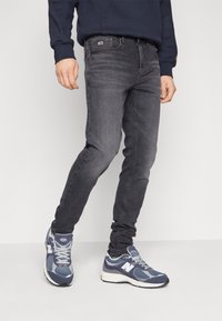 Smal passform grå jeans med en subtilt blekt design, fem fickor och en märkeslapp på midjan. Bärs med marinblå sportskor.