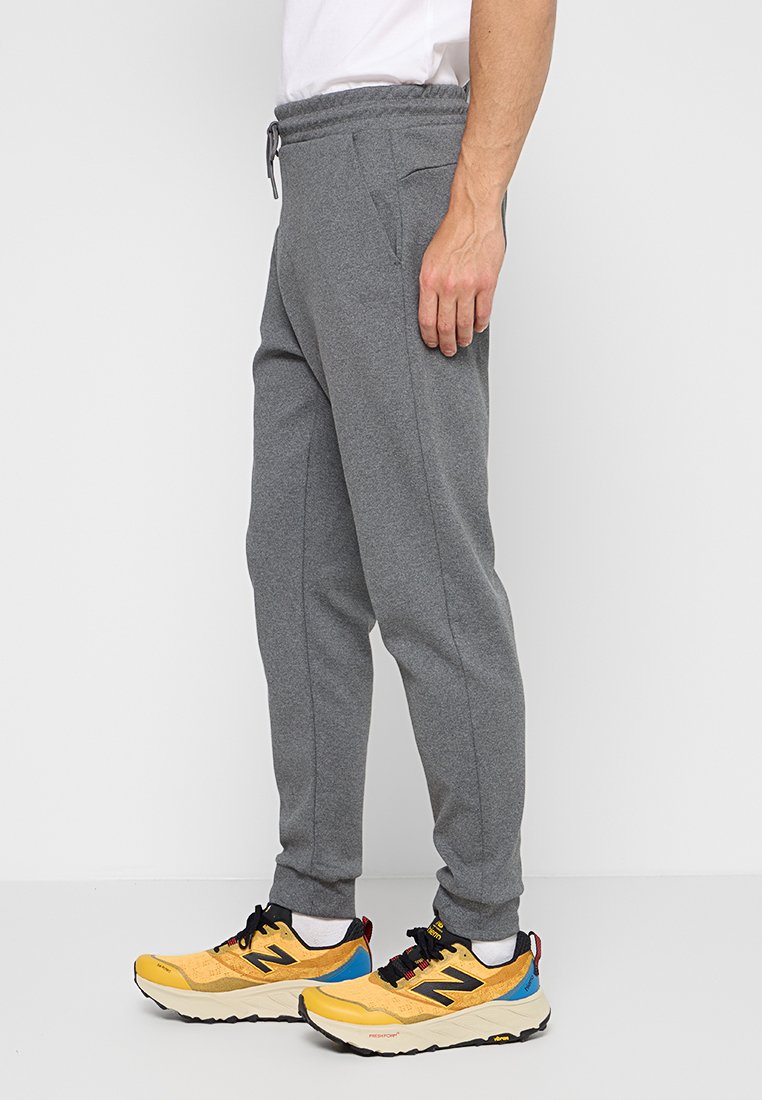 Pantaloni tuta grigi con vita elastica, tasche laterali e vestibilità affusolata. Indossati con scarpe da ginnastica gialle e nere.