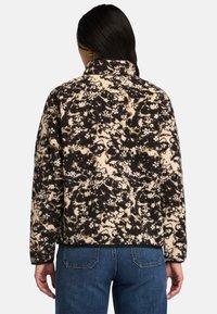 Fleecejacka med blommönster i beige och svart, med hög krage och avslappnad passform, ihop med blå jeans.