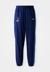 Marineblaue Jogginghose mit elastischem Bund, versehen mit einem Vereinslogo auf dem linken Oberschenkel und einem gelben Nike-Swoosh auf der rechten Seite.