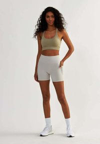 Soutien-gorge de sport beige et short taille haute gris clair avec poches, associés à des chaussures de sport blanches et des chaussettes montantes blanches.